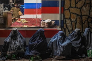 Afghan burqa-clad women sit in front of a bakery as they seek alms in Kabul