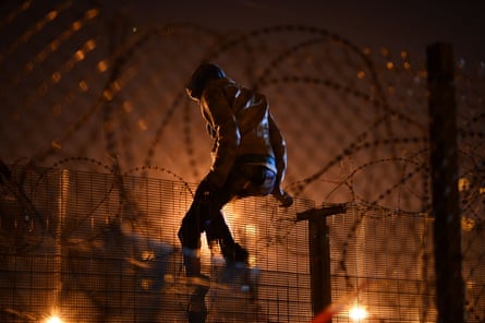 A migrant camped attempts to climb a security fence near refugee camp of Calais