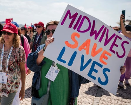 Woman walk down down a sunny street with one holding a sign saying ‘midwives save lives’.