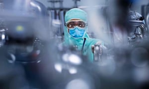 A lab technician, wearing personal protective equipment, prepares stainless steel tanks for manufacturing vaccines