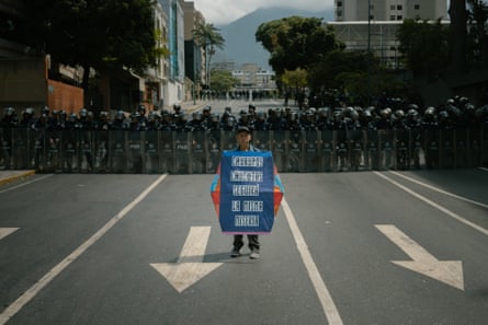 a man stands with a sign in front of a line of riot police