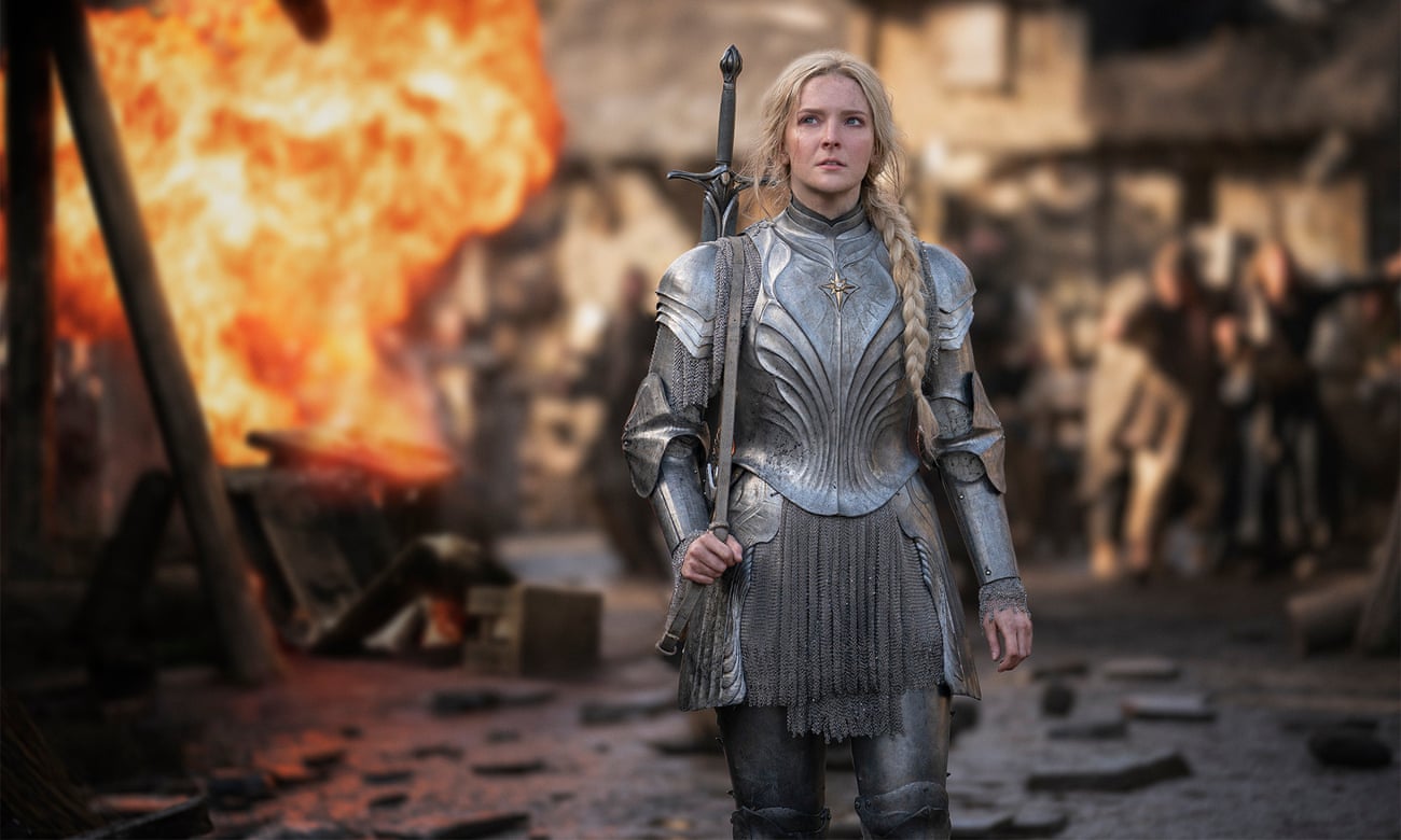 Morfydd Clark as Galadriel, wearing armour, holding a sword, with an explosion behind her.