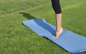 A woman standing on tip toe on a yoga matt in a field.