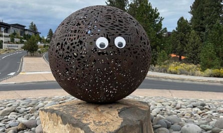 Googly eyes on a round metal sculpture poised on a stone in a park.