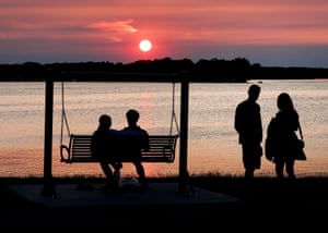 Four people in silhouette, with two of them seated on a swing, against a deep red sunset