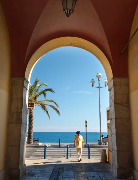 Sunny view to the sea and palm tree, with a pan crossing the road in front, through Archway on Promenade des Anglais