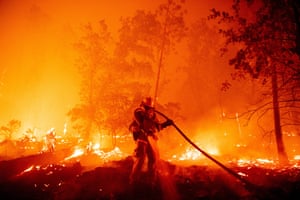 A firefighter surrounded by trees and burning cinders sprays water from a hose