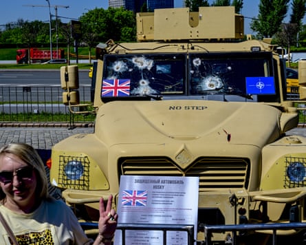 A woman posing with a peace hand-sign in front of a British military truck.