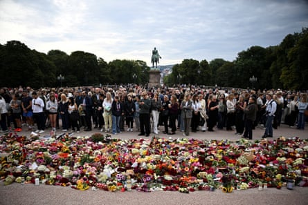 People gather behind a large collection of flowers laid on the ground with a statue in the background