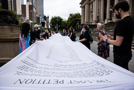 Protesters are seen holding The Lost Petition artwork by artist Dans Bain, showing the names of women and children killed by violence, as they participate in a Women’s March 4 Justice in Melbourne, Sunday, February 27, 2022.