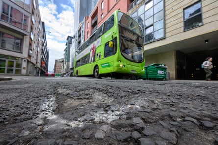 A lime green bus on a road in Bristol filled with holes and tarmac ripped up
