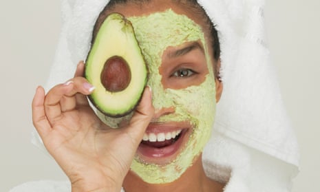 A young woman wearing a facial mask holding a slice of avocado