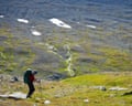 A hiker with a backpack and poles climbs a slope above Sarek's snow-patched valley, Arctic Sweden