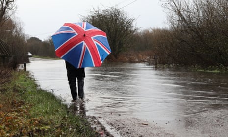 A person under a Union Jack umbrella attempts to walk along the flooded road at Sutton Gault in Cambridgeshire, in December.