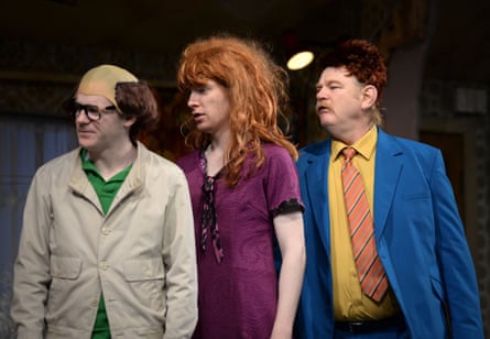 A man in a trench coat with a fake bald head, a man wearing a red wig and a purple dress, and a man in a blue suit with a yell0w shirt and a patterned tie
