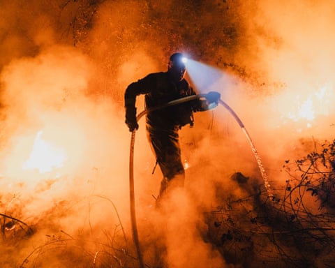 A forest brigadier uses a hose to extinguish flames