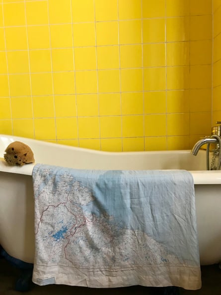 Orsola de Castro’s map dress draped over the side of a bath with a yellow tiled wall behind.