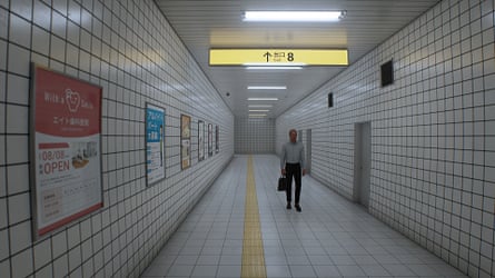 A game screenshot: a long corridor in the Tokyo metro, a person walking towards the camera.