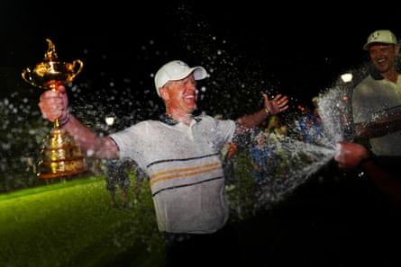 Captain Luke Donald is sprayed by champagne while holding the Ryder Cup trophy.