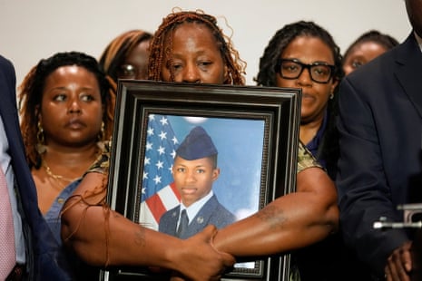 An older woman holds a framed photo of a young airman in uniform.