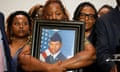 A grieving mother holds a large photo of her son in front of other relatives.