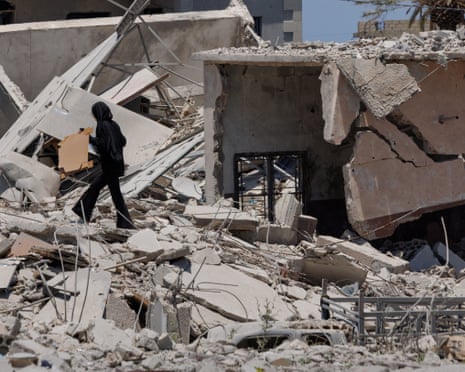 A woman holds belongings as she walks among the rubble of a neighbourhood completely destroyed by an Israeli airstrike, after the US and Iran deal, in Qlailieh, Tyre district, Lebanon.
