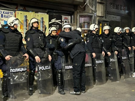 A celebrating person embraces a riot police officer amid a line of helmeted officers with shields