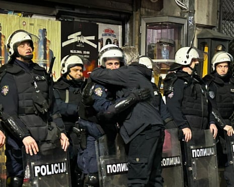 A celebrating person hugs a riot police officer as others stand holding shields, in Belgrade
