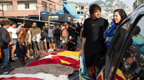 People look at a line of bodies covered in blankets laid out on a street