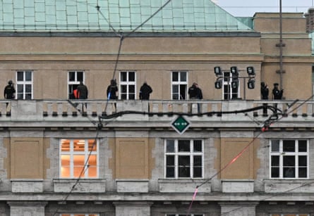 Several black-clad figures on a long, wide stone balcony of an old building, seen from a distance
