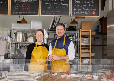 A man and a woman in yellow aprons stand behind the counter of fishmongers