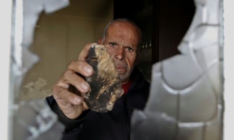 Qasem Suleman al-Fukaha shows a stone through a broken hole in his window