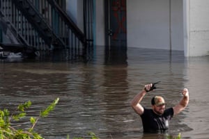 a man holds a walkie-talkie as he walks through chest-high water