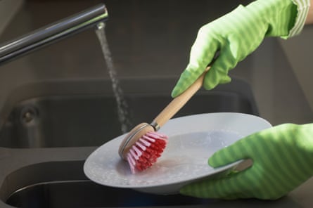 Hands wearing rubber gloves do the washing-up at a sink.