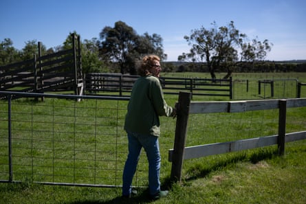 Woman opening farm gate with paddock and trees in background.