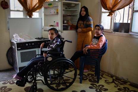 Aisha Ibrahim stands next to her nearly empty fridge with two of her three disabled children, Zam Zam and Bayan, at their new home in in Zahlé, 25 March 2021