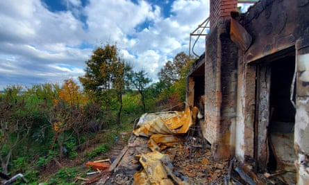 A burnt-out house with no windows and buckled metal roofing on the ground