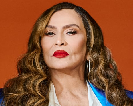 Tina Knowles in a cream blouse and trousers, and a long blue coat