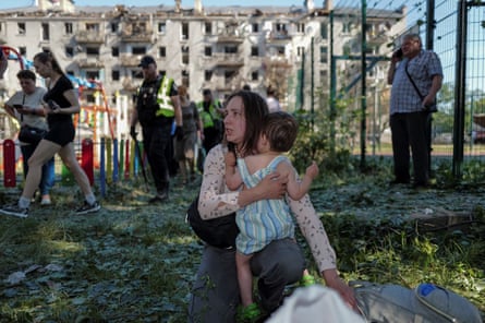 A woman holds a child near an apartment building damaged during the Russian missile and drone strike in Kyiv.