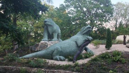 A lifesize model of two grinning crocodile-like creature, in a leafy park setting