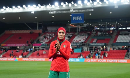 Nouhaila Benzina of Morocco stands on the pitch, frowning and hands pressed together, wearing a T-shirt, shorts and hijab