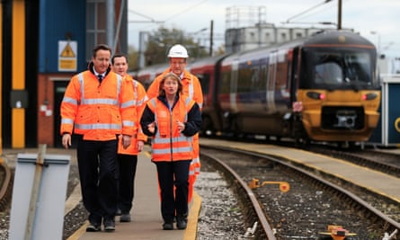 Cameron visits an East Midlands train depot with Osborne – the pair with two railway officials walking down a platform, all wearing bright orange hi-vis jackets, with train in background