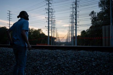 A man stands outside with many power lines overhead.