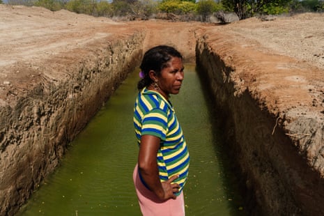 A woman stands in front of a long, deep trench a third full of green water