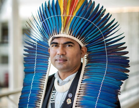 A man in a headdress of blue and yellow feathers wears a western-style jacket with Indigenous necklaces 
