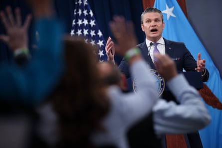 A man next to a US flag speaks to a crowd of people raising their hands