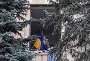 A man holds a Ukrainian national flag as he stands at the window of a damaged administrative building in Kharkiv
