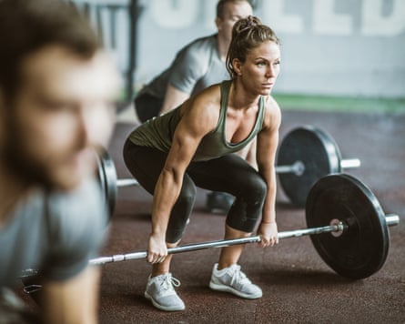 Group of athletic people exercising deadlift with a barbell in a health club. The focus is on a woman.