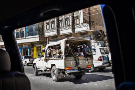 The photograph is taken from inside a car. Outside the car window we can see a  military truck of Houthi militiamen.