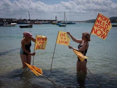Two women in the sea at St Ives, Cornwall, UK, with banners protesting at second-home ownership made by local artist Camilla Dixon (on left)